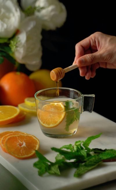 pexels-photo-20258244-20258244 A close-up of honey being drizzled into a cup of citrus tea with mint and orange slices.