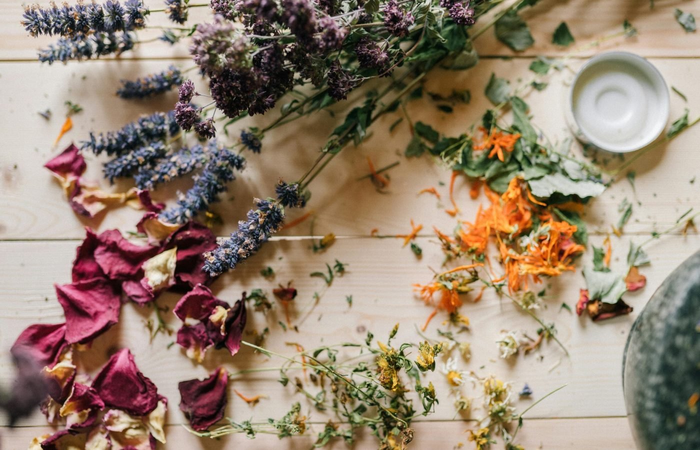 pexels-photo-5480162-5480162 Assorted dried flowers and herbs scattered on a wooden table with a ceramic bowl.